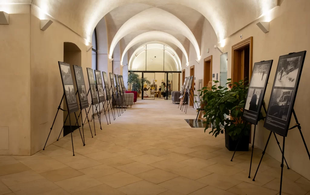 Dlouhá chodba s klenutými stropy má na obou stranách několik vystavených fotografií na stojanech, které připomínají Velkou putovní výstavu. Rostliny jsou umístěny přerušovaně mezi displeje. Lidé jsou vidět v místnosti na konci.